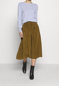Light blue sweater with textured knit, paired with a pleated, knee-length mustard skirt. Black ankle boots complete the outfit.