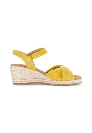 Gul kile-sandal med flettet snore sål, åben tå, knude foran rem og justerbar ankelrem på hvid baggrund.