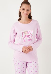 Világos rózsaszín, hosszú ujjú póló, amelyen a "DONUT WORRY BE HAPPY" felirat található, világos rózsaszín és lila árnyalatú pöttyös pizsama nadrággal párosítva. Puha pamutszövetből készült.