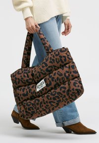 Braune Puffer-Tasche mit schwarzem Leopardenmuster. Verfügt über robuste Griffe und ein Etikett mit der Aufschrift "SENSES THE LABEL." Texturiertes, gesteppte Design.