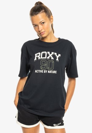 Black cotton t-shirt with short sleeves and a relaxed fit. Features “ROXY 90 ACTIVE BY NATURE” printed in contrasting white and green text.