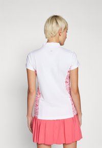 Poloshirt in Weiß mit rosa Blumen-Seitenpaneelen. Kurze Ärmel, Kragen und gerade Säume. Glatte Textur, athletischer Schnitt, minimaler Hardwareeinsatz.