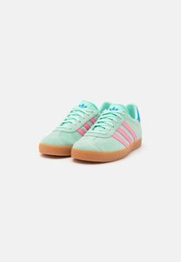 Grønne semskede sneakers med rosa striper, blå detaljer og såle av gummi. Har snøring foran og polstret krage.