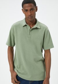 Lichtgroene polo met korte mouwen, voorzien van een gestructureerde afwerking, een geknoopte kraag en een losse pasvorm. Gedaagd met blauwe spijkerbroek.