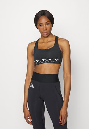 Sutiã desportivo preto com detalhe de logotipo branco, apresentando um decote em forma de sorriso e alças largas, combinado com leggings pretas de cintura alta.