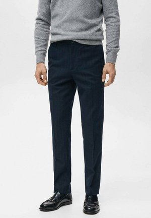 Pantalon à fines rayures bleu marine en tissu léger, coupe ajustée, associé à des chaussures en cuir noir et un pull en maille gris.