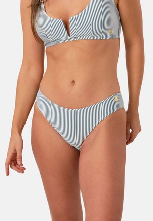 Kvinde iført blå og hvide vertikale stribede bikini med gyldne cirkulære accenter på top og bund mod en ensartet lys baggrund.