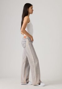  Τζιν παντελόνι σε ανοιχτό γκρι χρώμα με φαρδιά πόδια και ξεθωριασμένη υφή, διαθέτει κλασικό σχεδιασμό με πέντε τσέπες και δερμάτινη ετικέτα στο πίσω μέρος.