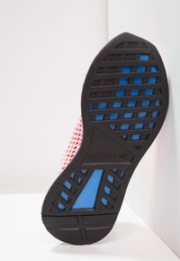 Semelle en caoutchouc noir avec accents bleus ; tige en maille rouge vif ; présente un motif texturé et une conception de ventilation pour la respirabilité.