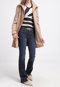 Beige mid-lengte jas over een zwart-wit gestreept topje, gecombineerd met donkerblauwe flared jeans en beige puntige ballerina's. Eenvoudig ontwerp en texturen.