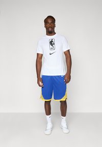 Hvit t-skjorte med korte ermer og svart NBA-logo og Nike-logo, i kombinasjon med blå knelengde shorts med gule sidestriper. Hvite sneakers.