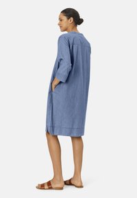 Chambray-mekko, polvenpituinen, jossa on kolme neljännesosaa hihat ja sivutaskut. Väri on vaaleansininen ja pinnassa on sileä rakenne. Yhdistetty ruskeisiin sandaaleihin.