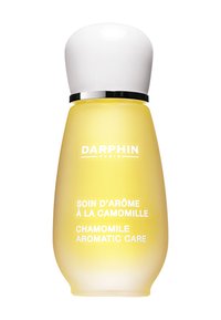 Bouteille en verre jaune de forme arrondie, avec un capuchon blanc et un bandeau argenté. L'étiquette présente un texte blanc : "Soins Aromatiques à la Camomille" en français et en anglais.