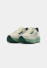 Baskets de sport crème et vert avec une tige texturée, des accents contrastants en vert foncé, et une semelle flexible et rembourrée.