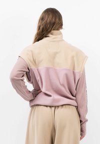 Fleece-Pullover mit hohem Kragen; beiger Oberteil und pinker Unterteil; mit Raglanärmeln und strukturiertem Stoff.