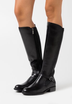 Bottes en cuir noir montantes jusqu'aux genoux avec un panneau texturé, une fermeture éclair latérale et un petit accent de boucle au niveau de la cheville. Design à semelle plate.