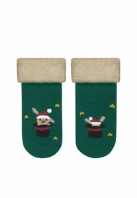 Grüne Socken mit einem flauschigen, beigen Saum. Das Design zeigt einen Cartoon-Hasen in einem Zauberhut, akzentuiert mit gelben Sternen.