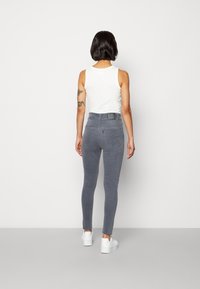 Jeans ajustados grises de denim, con una cintura alta, sutiles bolsillos traseros, combinados con una camiseta sin mangas blanca y zapatillas blancas.