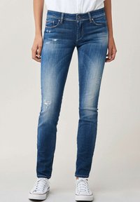 Jean skinny en denim bleu avec des détails déchirés et un léger délavage. Doté d'un bouton de fermeture, de passants de ceinture et d'un design classique à cinq poches.