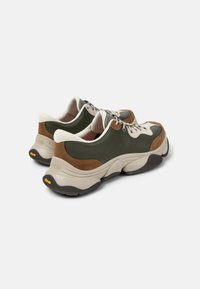 Vihreät ja ruskeat nahkakengät, joissa on pehmeä harmaa pohja ja beige yksityiskohtia. Kengissä on nauhaketju ja Vibram-logot ulkopohjassa.