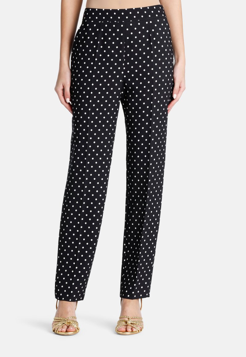 Pantalons noirs à pois blancs, avec une coupe droite, une texture lisse et une taille, associés à des sandales dorées à lanières.