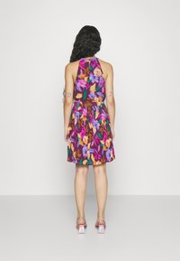 Woman with long black hair wearing a sleeveless purple floral dress and pink block-heeled sandals, shown from the back.