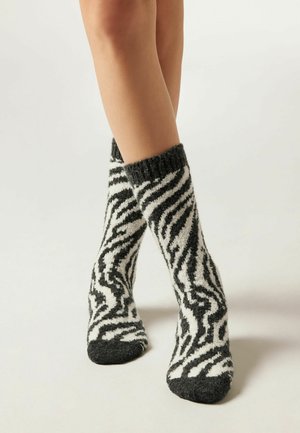 Chaussettes à rayures noires et blanches avec une texture duveteuse, présentant un bord côtelé et un design ressemblant à des motifs de zèbre.