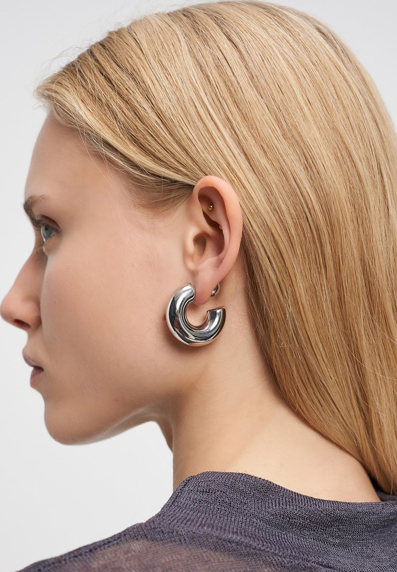 Silberfarbene Metall-Hoops mit einem verdrehten Design, die eine glatte, reflektierende Oberfläche und eine leicht kreisförmige Form aufweisen.