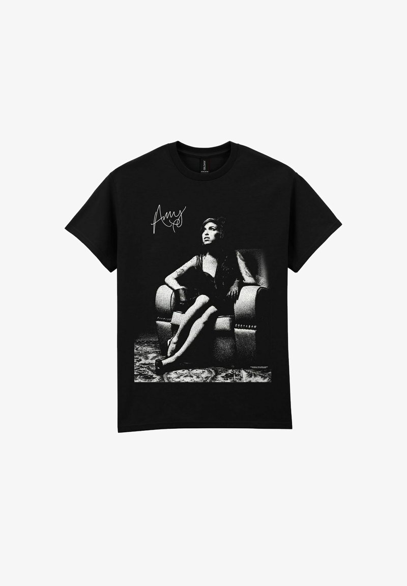 Camiseta de algodón negra con un gráfico en blanco y negro de una mujer sentada con una firma encima de la imagen, sobre un fondo estampado.