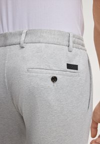 Graue Jogging-Shorts mit elastischem Bund, einer Gesäßtasche mit einem schwarzen Knopf und einem Etikett, aus strukturiertem Stoff.