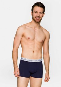 Granatowe bokserki stretch z białą, markową gumką w talii. Materiał jest gładki, a krój przylegający do ciała. Model stoi pewnie na jednolitym tle.