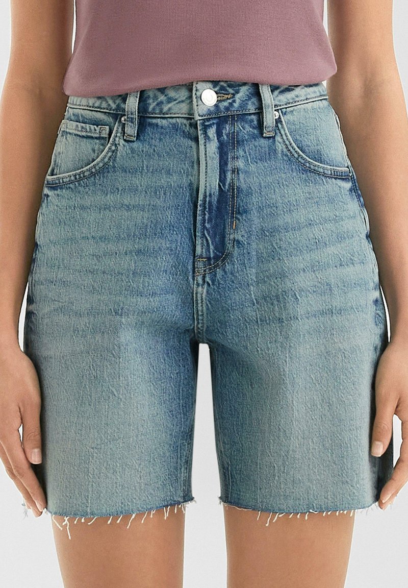 Shorts en denim bleu clair, taille haute, avec un ourlet effiloché, des poches avant et une fermeture à bouton en métal.