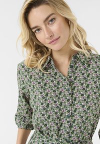 Grön blommig skjortklänning med krage, prydd med små rosa och vita blommor, knappstängning fram och uppvikta ärmar. Mjuk tyg med en flödande design.