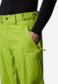 Lime gröna byxor gjorda av slitstarkt tyg, med framfickor, knappstängning och en DRYVENT-logotyp på midjebandet.