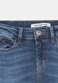 Denimjeans i en mörkblå tvätt med orange sömmar, med en knappstängning, logotagg och framfickor.