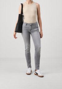 Vaqueros ajustados grises de cintura media, combinados con una blusa sin mangas beige y zapatillas blancas con detalles negros. Bolsa tote negra al hombro.