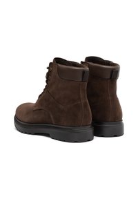 Par de botas de ante marrón hasta el tobillo con suelas de goma negras, cordones en la parte delantera y cuello acolchado, vistas desde la parte trasera sobre un fondo blanco.