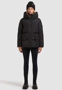 Mustkunst must jacket suure kapuutsiga, varrukate tõmblukk, kaks eesmist taskut ja nööridetailid, koos mustade retuusidega ja lahingusaabastega.
