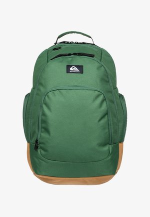 Grøn og brun Quiksilver rygsæk med flere lynlåslommer og et topgreb, vist mod en hvid baggrund.