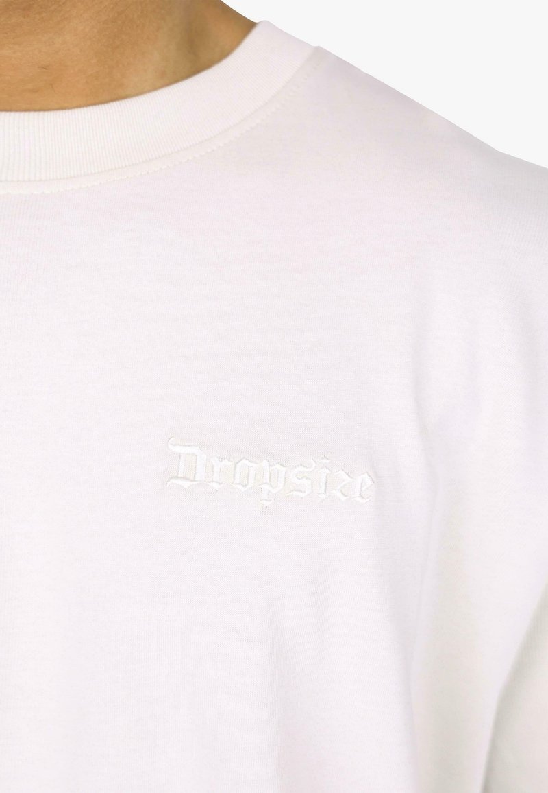 White cotton t-shirt featuring a round neckline and small embroidered "Dropsize" logo in matching white thread on the chest.