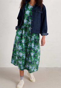 Robe florale verte avec des accents bleus et noirs, associée à une veste en denim foncé. Des baskets blanches complètent l'ensemble.