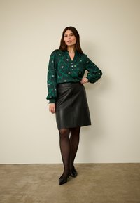 Green patterned blouse with puffed sleeves, paired with a black leather pencil skirt. The outfit features a structured fit and sleek textures.