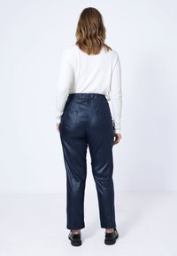 Marine faux leren broeken met een gladde textuur, elastische tailleband en twee achterzakken, van achteren weergegeven met een wit lang%mouwen top.