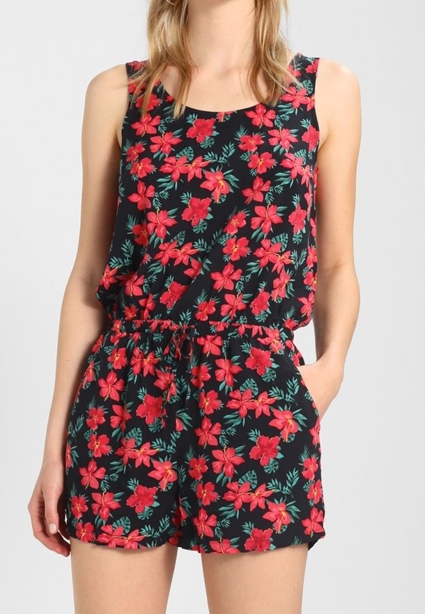 Combinaison noire sans manches avec imprimé floral rouge et feuilles vertes, dotée d'une taille à cordon et de poches latérales, portée par une femme aux cheveux blonds.