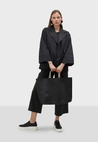 Černá kožená tote taška s texturovaným povrchem, s dvojitými uchy a kontrastními grafickými popruhy. Nosit s volným černým oblečením a platformovými botami.