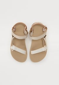 Beige Sandalen mit einer strukturierten Sohle, ausgestattet mit weißen Stoffriemen und verstellbaren Verschlüssen an Knöchel und Zehen. Flaches Design, offener Zeh.