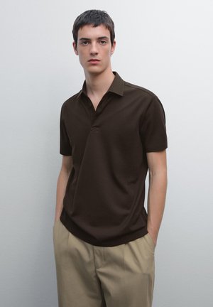 Bruine polo met korte mouwen, voorzien van een platte kraag, een relaxte pasvorm en subtiele stiksels, gecombineerd met beige broeken.