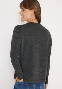 Maglione lavorato a maglia grigio scuro, colletto a girocollo, maniche lunghe, motivo a spina di pesce testurizzato, vestibilità rilassata, vista posteriore con le mani nelle tasche.