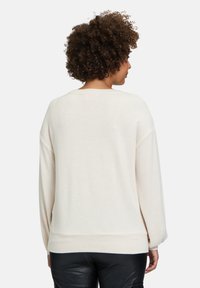 Helles beiges, übergroßes Sweatshirt mit rundem Halsausschnitt, überschnittenen Schultern und geripptem Saum. Weicher Strickstoff und legere Silhouette.