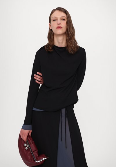 Sort langærmet top med høj hals og en løs pasform, lagd over en mørkeblå nederdel. Holder en bordeaux læderclutch.